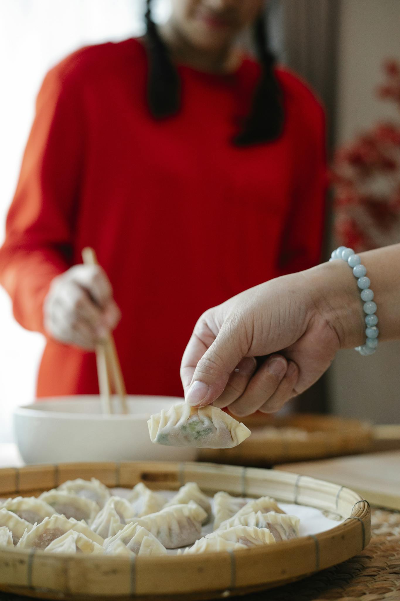 Anonymous mother and daughter preparing Chinese jiaozi dumplings in kitchen